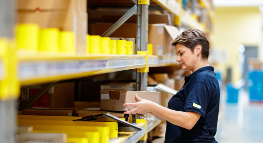 Warehouse worker handling a cardboard box beside industrial storage shelving